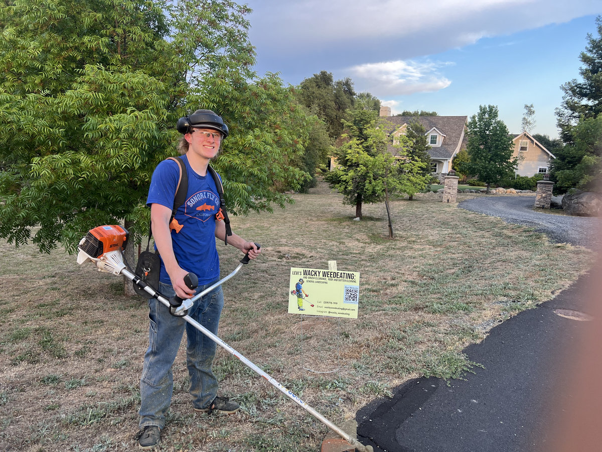 Crew member with weed eater next to Wacky Weedeating sign