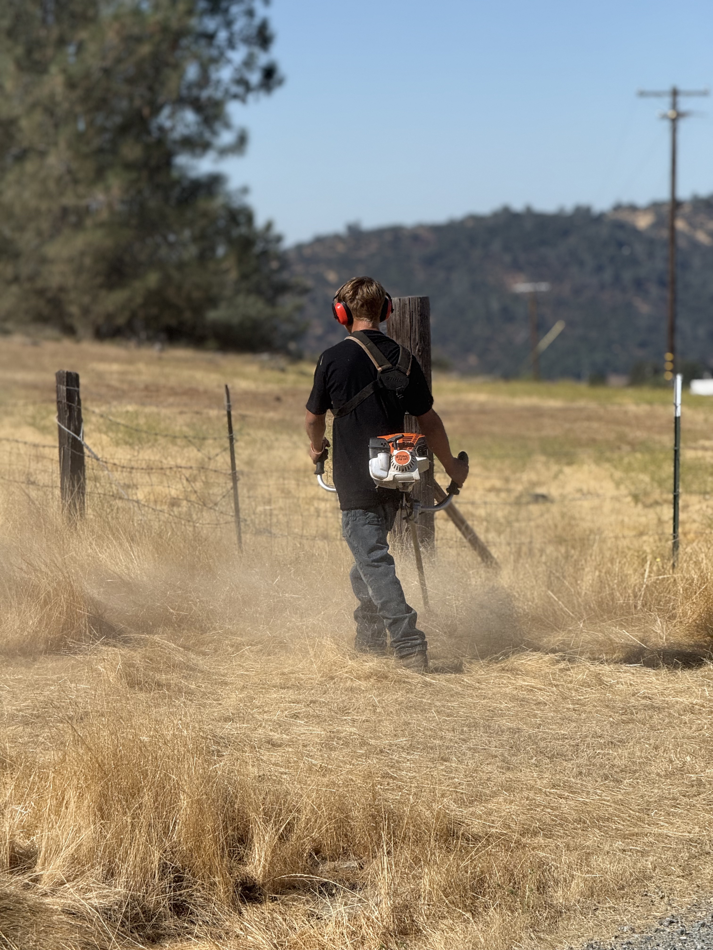 Crew member weed eating along a hillside fence line